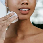 Imagem de uma modelo de cor negra limpando a pele com algodão ilustrando o texto A pele humana: estrutura, funções, tipos e características