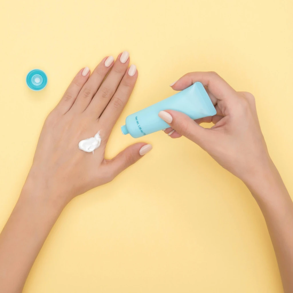 Imagem com uma mão segurando um bastão de protetor solar e passando em sua outra mão sobre um fundo amarelo ilustrando o texto Descubra as diferenças entre protetor, bloqueador e filtro solar.