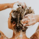 Imagem de uma mulher com cabelos claros de costa usando um shampoo em barra clean beauty ilustrando o texto Conheça os tipos de shampoos clean beauty e como cada um pode transformar o seu cabelo publicado no site Simplicity