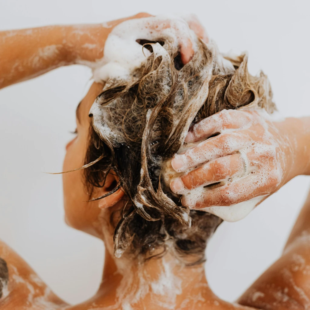 Imagem de uma mulher com cabelos claros de costa usando um shampoo em barra clean beauty ilustrando o texto Conheça os tipos de shampoos clean beauty e como cada um pode transformar o seu cabelo publicado no site Simplicity