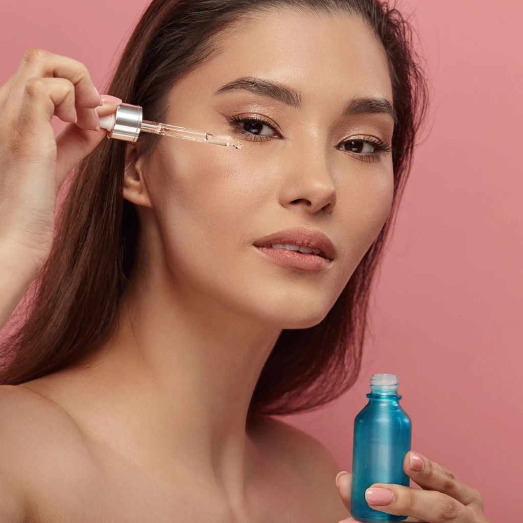 Imagem de uma mulher com traços orientais pingando cosmético em seu rosto ilustrando o texto O que não usar com ácido retinoico