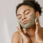 Close de um rosto feminino de pele morena aplicando cosmético ilustrando o texto Argila: saiba o que é, origem, os diferentes tipos , usos e benefícios