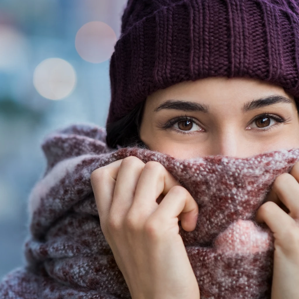 Imagem de uma mulher com roupas de inverno cobrindo parte debaixo do rosto em proteção ao frio