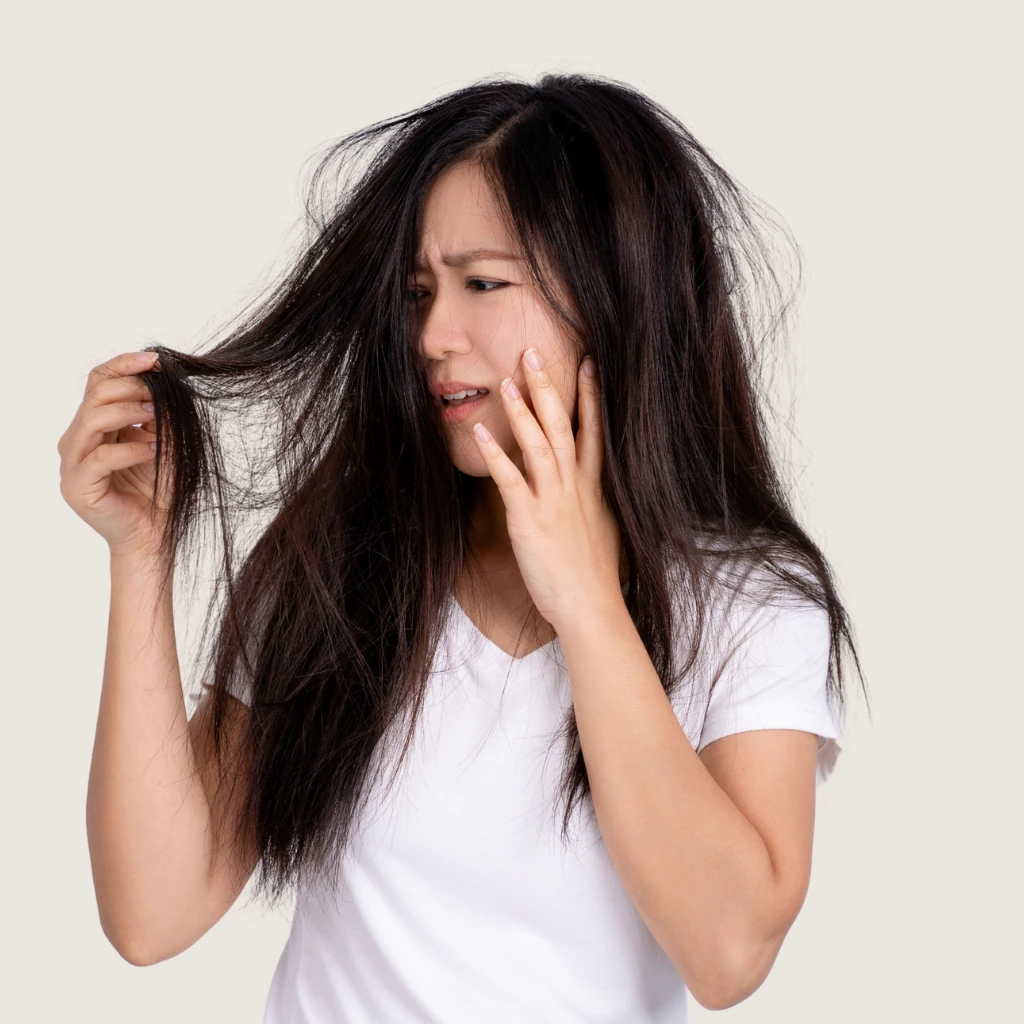 Imagem de uma mulher de pele branca segurando o cabelo com uma expressão de desespero pelo cabelo com problemas