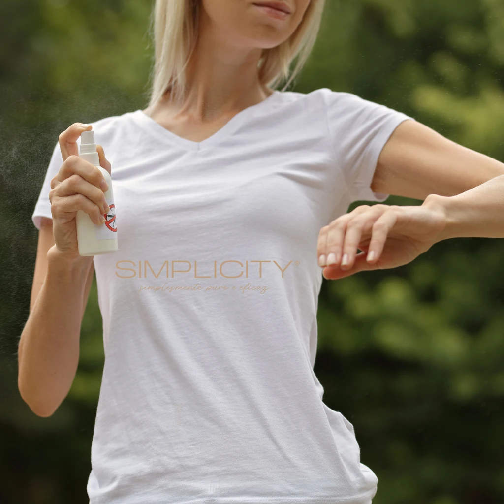 Imagem de uma mulher vestindo uma camiseta branca aplicando repelente sobre a pele do braço esquerdo